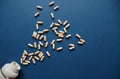 White and yellow capsules spill out of an overturned white bottle with pills on blue background. Royalty Free Stock Photo