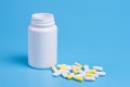 White and yellow pills, tablets and white bottle on blue background