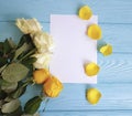 White and yellow roses on a blue wooden background place for text blank white card