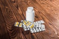 White and yellow tablets or vitamins and closed white medicine bottle on a wooden table.