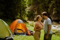 White young couple smiling and talking to each other by tent in forest