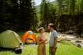 White young couple smiling and talking to each other by tent in forest