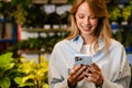 White young florist girl smiling and using cellphone in flower shop Royalty Free Stock Photo