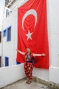 A white young girl tourist in red clothes with a backpack is standing and smiling against the background of a building with a hug