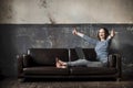 White young woman in jeans and a vest sitting on the couch with a laptop and happy, shows the sign class