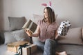 White young woman with pink rabbit ears on her head sitting on the couch with gift boxes and smiling, girl in pink blouse and Royalty Free Stock Photo