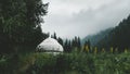 white yurt, a nomad house in a mountain forest meadow among grass and flowers in rainy and foggy weather Royalty Free Stock Photo