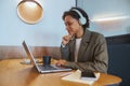 A whitecollar worker with headphones is using a laptop at a desk