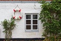 Whitewashed brick wall with window, green bushes and red and white life buoy Royalty Free Stock Photo