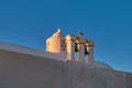 Whitewashed Greek Orthodox chapel, small belfry with cross and bell, roof and dome at sunset sky background. Close-up Royalty Free Stock Photo