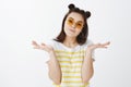 Who cares, relaxed and chill. Stylish carefree young woman in sunglasses and yellow t-shirt, shrugging and spread hand