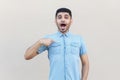 Who? me? Portrait of surprised handsome young bearded man in blue shirt standing, pointing himself and looking at camera with Royalty Free Stock Photo