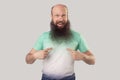 Who? me? Portrait of surprised middle aged bald man with long beard in light green t-shirt standing, pointing himself and looking Royalty Free Stock Photo
