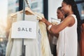 Who said money cant buy happiness. two women looking at dresses on a rail with a sign that reads sale. Royalty Free Stock Photo