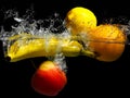 Whole banana, orange, lemon and apple in water on a black background. Fresh fruit with water spray Royalty Free Stock Photo