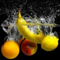 Whole banana, orange, lemon and apple in water on a black background. Fresh fruit with water spray Royalty Free Stock Photo