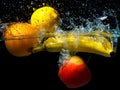 Whole banana, orange, lemon and apple in water on a black background. Fresh fruit with water spray Royalty Free Stock Photo