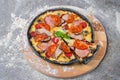 Black dough Pizza with meat slices, salami, ham, sliced tomatoes, mozzarella cheese served with fresh basil leaf on wooden plate Royalty Free Stock Photo