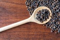 Whole black pepper balls in wooden spoon, wooden background Royalty Free Stock Photo