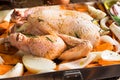 Whole chicken seasoned uncooked in baking tray with chopped vegetables carrots potatoes onions, rosemary