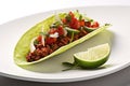 a whole chili pepper placed in a beef taco on a white plate, garnished with lime wedges