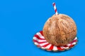 Whole coconut fruit on red and white striped plate with drinking straw on blue background