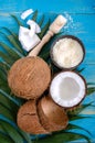 Whole coconut nut, shell, coconut flakes, green palm leaves on a blue wooden background. Top view, flat lay. Tropical theme