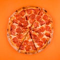 whole, cooked and sliced peperoni pizza on a bright orange background