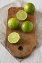 Whole and cut green citrus limes on a rustic wooden board over white wooden surface, side view. Close-up Royalty Free Stock Photo