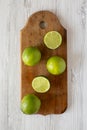 Whole and cut green citrus limes on a rustic wooden board over white wooden surface, top view. Flat lay, overhead, from above Royalty Free Stock Photo