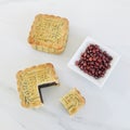 A whole and cut out a quarter moon cake in with red beans in a sauce dish on white marble background.