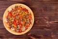 A whole delicious pizza with mushrooms, corn, cherry tomatos, courgettes and bell peppers on a round wooden plate