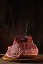 A whole freshly cut piece of raw pork loin lies on a cutting board with a stuck knife a brown wooden backdrop. side view. artistic Royalty Free Stock Photo