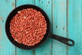 Whole fried pink peanuts in black cast iron pan on turquoise ta Royalty Free Stock Photo