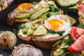 Whole grain bread sandwiches with fried quail egg, avocado, herbs and seeds on black background.