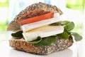 Whole grain bread with soft cheese, tomato and lamb`s lettuce on chopping board, close up.