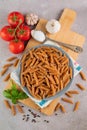 Whole grain flour penne pasta in a plate on a cutting board, basil, tomatoes, garlic, seasonings on a gray table. Cooking healthy Royalty Free Stock Photo