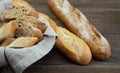 Whole-grain and traditional baguettes lie next to a wicker basket with a linen napkin and slices of bread. Wood background. Bakery