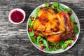 Whole grilled chicken on white dish with salad and cranberry