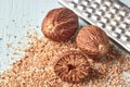 Whole and half nutmeg and grated nutmeg spice on background of metal grater on wooden light table