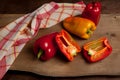 Whole and half red and yellow bell pepper on wooden background with red kitchen towel Royalty Free Stock Photo