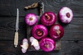 Whole and halfed Flat red sweet onion on a cutting board. Black Wooden background. Top View