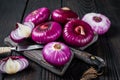 Whole and halfed Flat red sweet onion on a cutting board. Black Wooden background. Top View