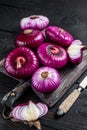 Whole and halfed Flat red sweet onion on a cutting board. Black Wooden background. Top View