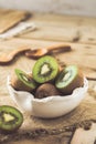 Whole and halfed kiwis in a white bowl on a rustic wooden table