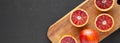 Whole and halved blood oranges on rustic wooden board over black surface, top view. Flat lay, overhead, from above. Copy space Royalty Free Stock Photo