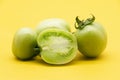 Whole and halved green unripe tomato isolated on yellow background Royalty Free Stock Photo