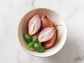Whole and halved red eschalots in a bowl over white marble background. Close-up of unpeeled long shallots. Ready for cooking