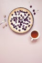 Whole homemade cherry cake on pastel pink background with fresh berries and cup of tea