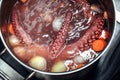 Whole octopus boiling in the the pot filled with water and vegetables. Tentacles of red octopus being boiled.